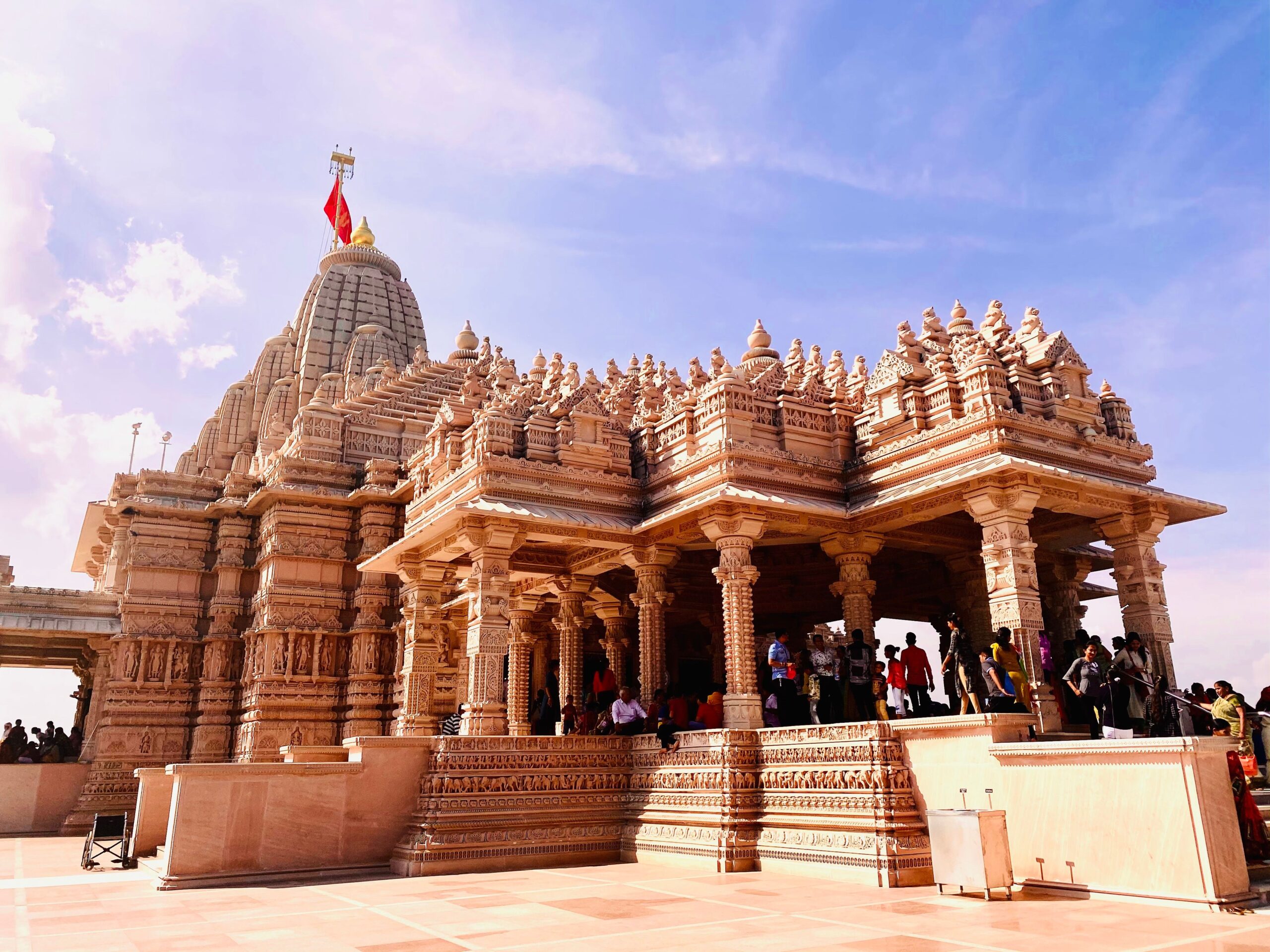 An impressive Hindu temple with detailed carvings and a vibrant flag under a clear blue sky.